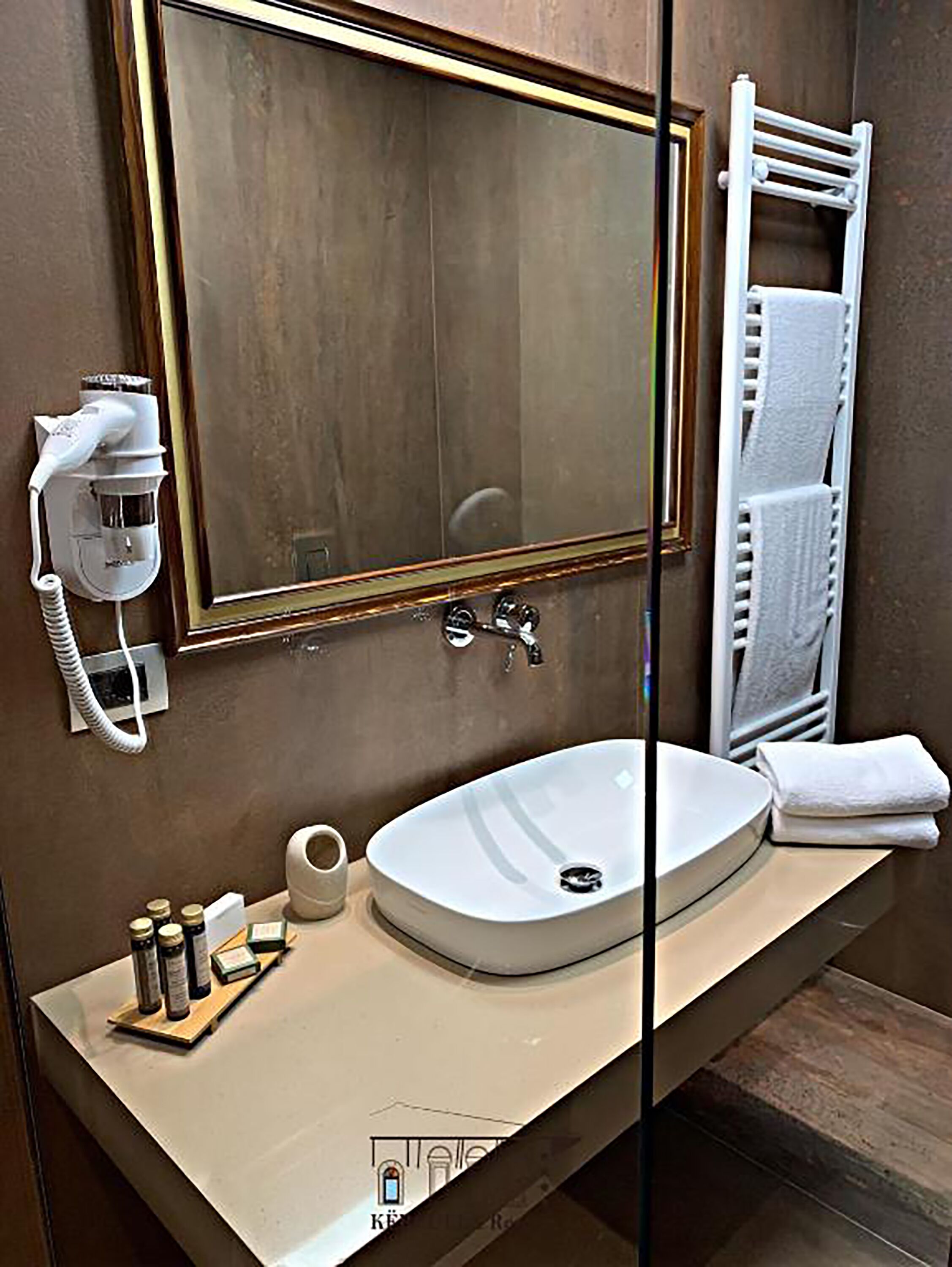 Ein Badezimmer mit großem Spiegel, Waschbecken, Handtuchhalter und Fön.