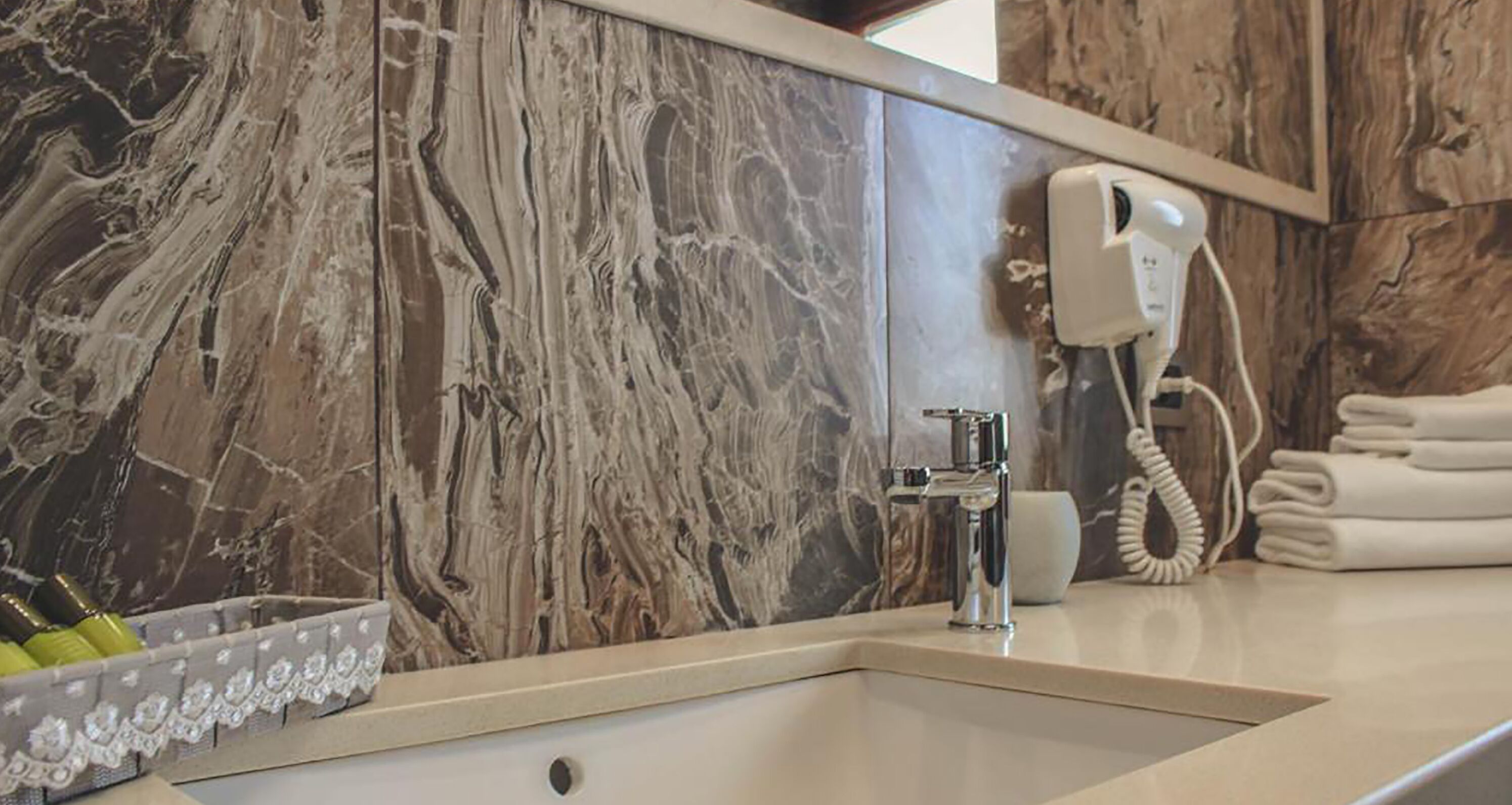 A bathroom with a marble wall, a sink, a hand dryer, and a towel rack.