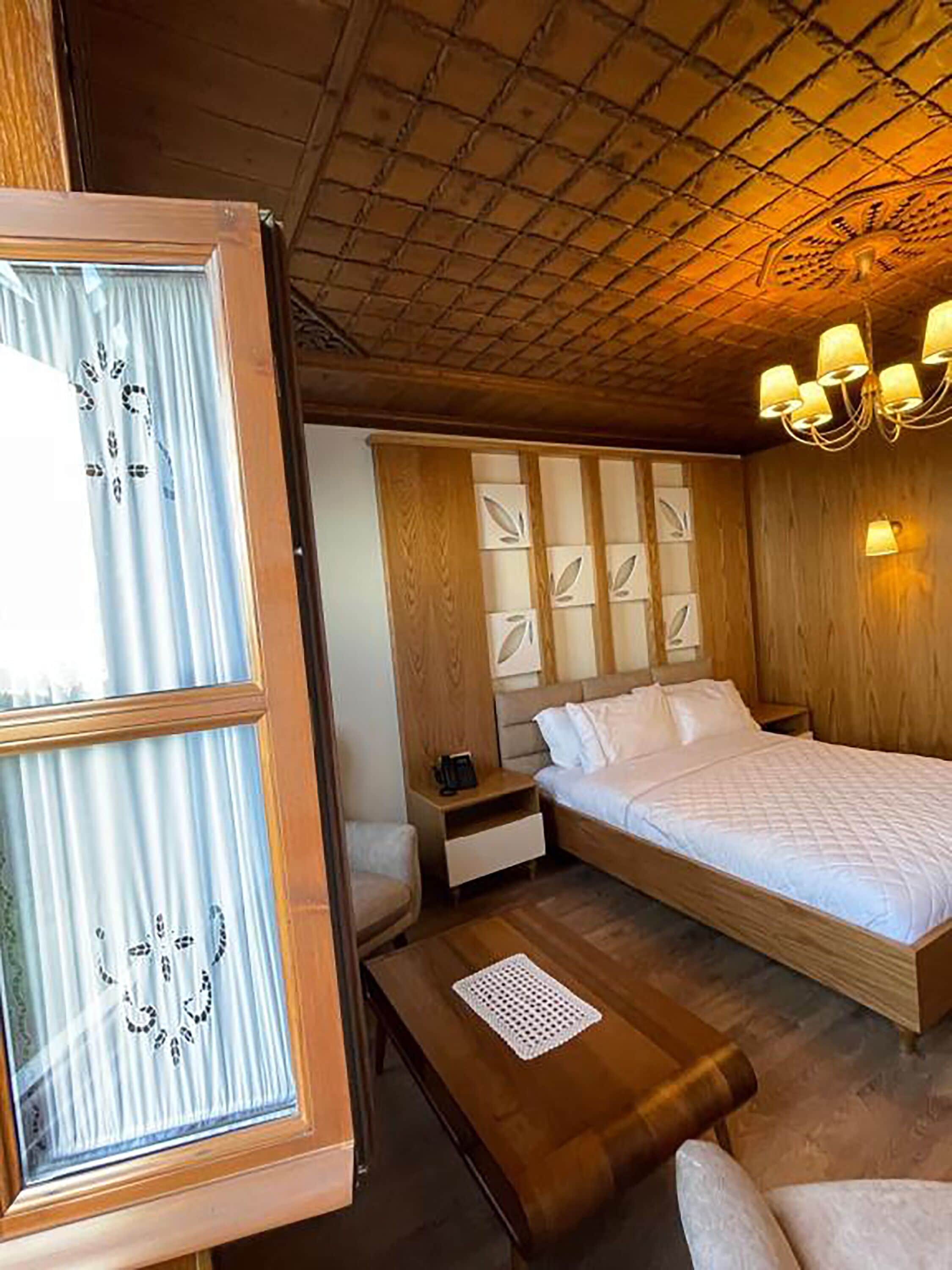 A room with a bed, a nightstand, a wooden headboard, a window with curtains, and a ceiling with a grid pattern.