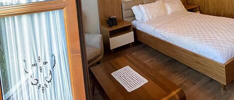 A room with a bed, a nightstand, a wooden headboard, a window with curtains, and a ceiling with a grid pattern.