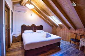 A bedroom with a wooden ceiling, a bed with white linens, a bedside table, and a small table with a chair.