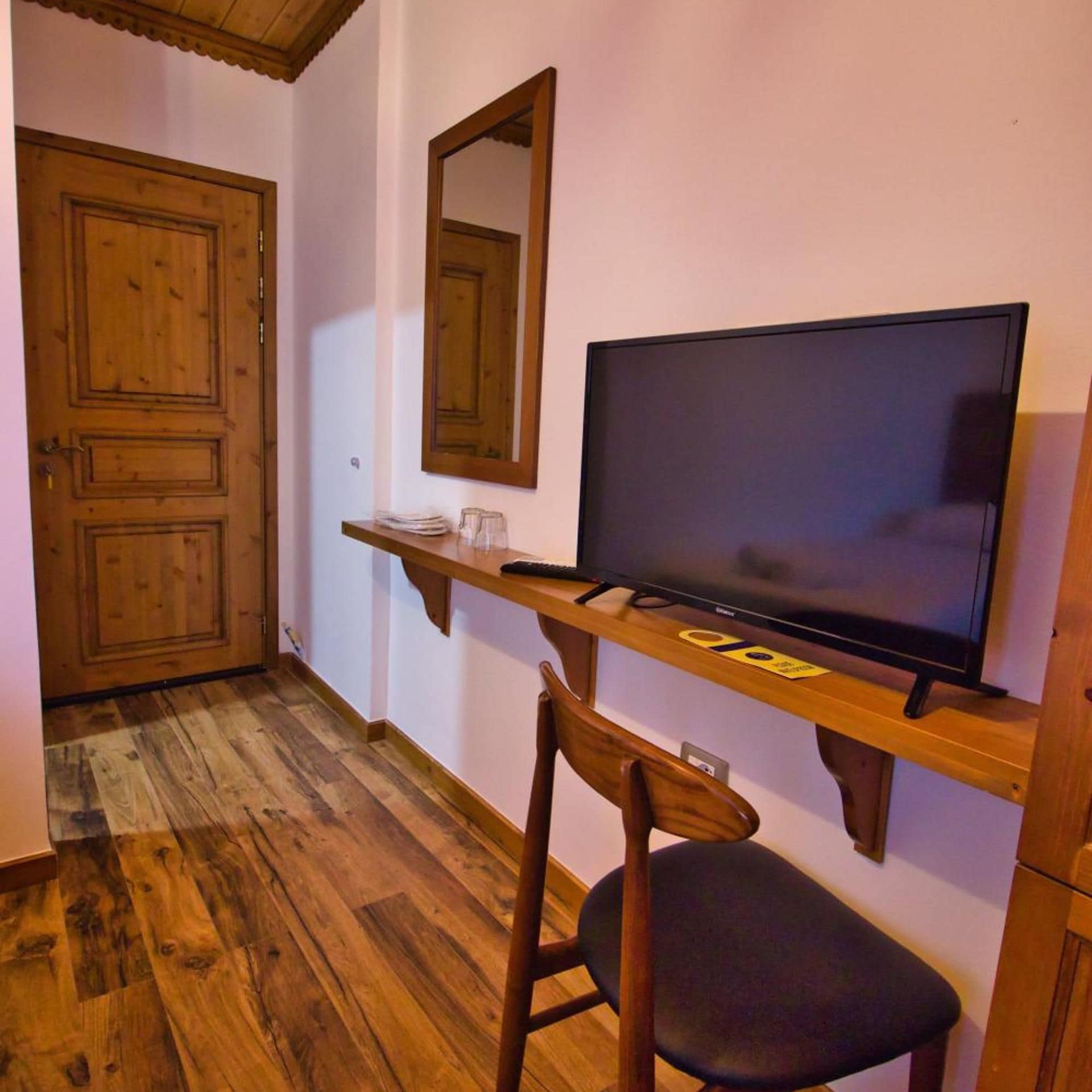 Una habitación con piso de madera, un televisor sobre un mueble de madera, una silla y una puerta.