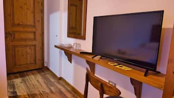 Una habitación con piso de madera, un televisor sobre un mueble de madera, una silla y una puerta.