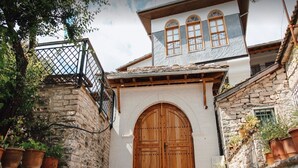 Ein traditionelles Steinhaus mit einer großen Holztür, einem Balkon mit Metallgeländer und Kübelpflanzen an den Wänden.