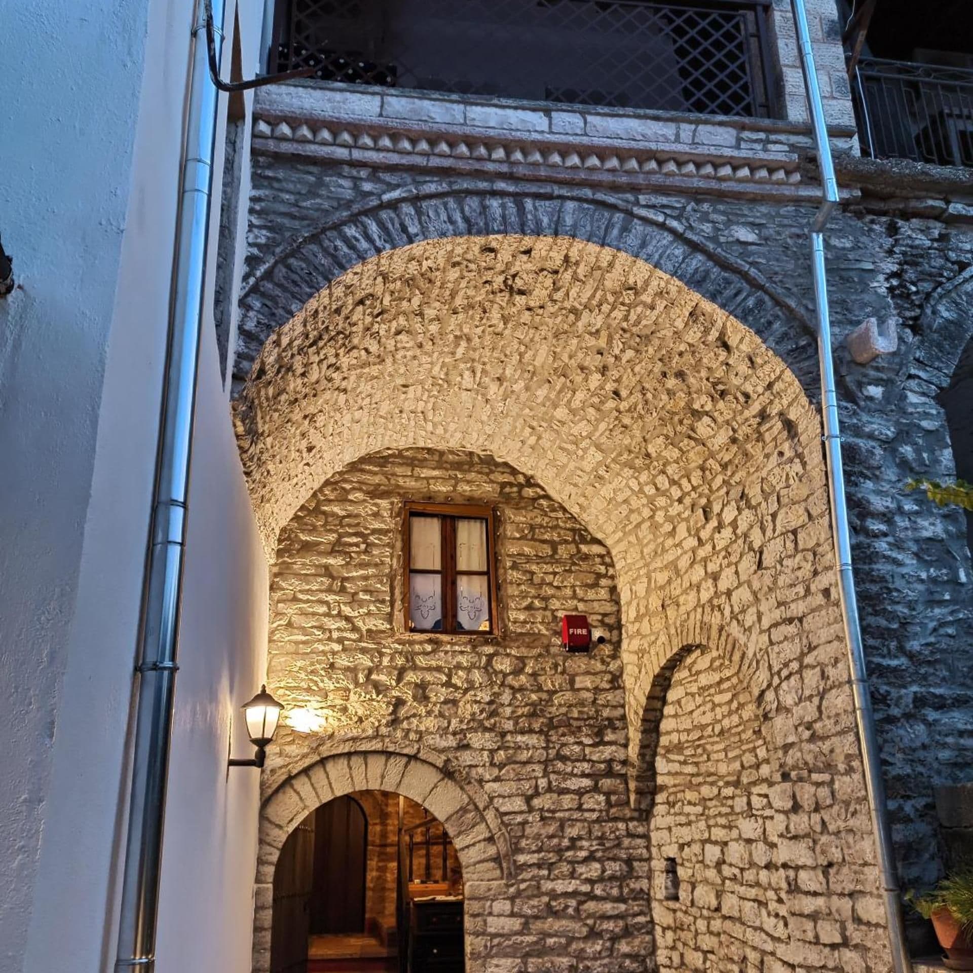 Un arco de piedra que da paso a una habitación con una puerta de madera, una ventana con cortina y un detector de incendios en la pared.