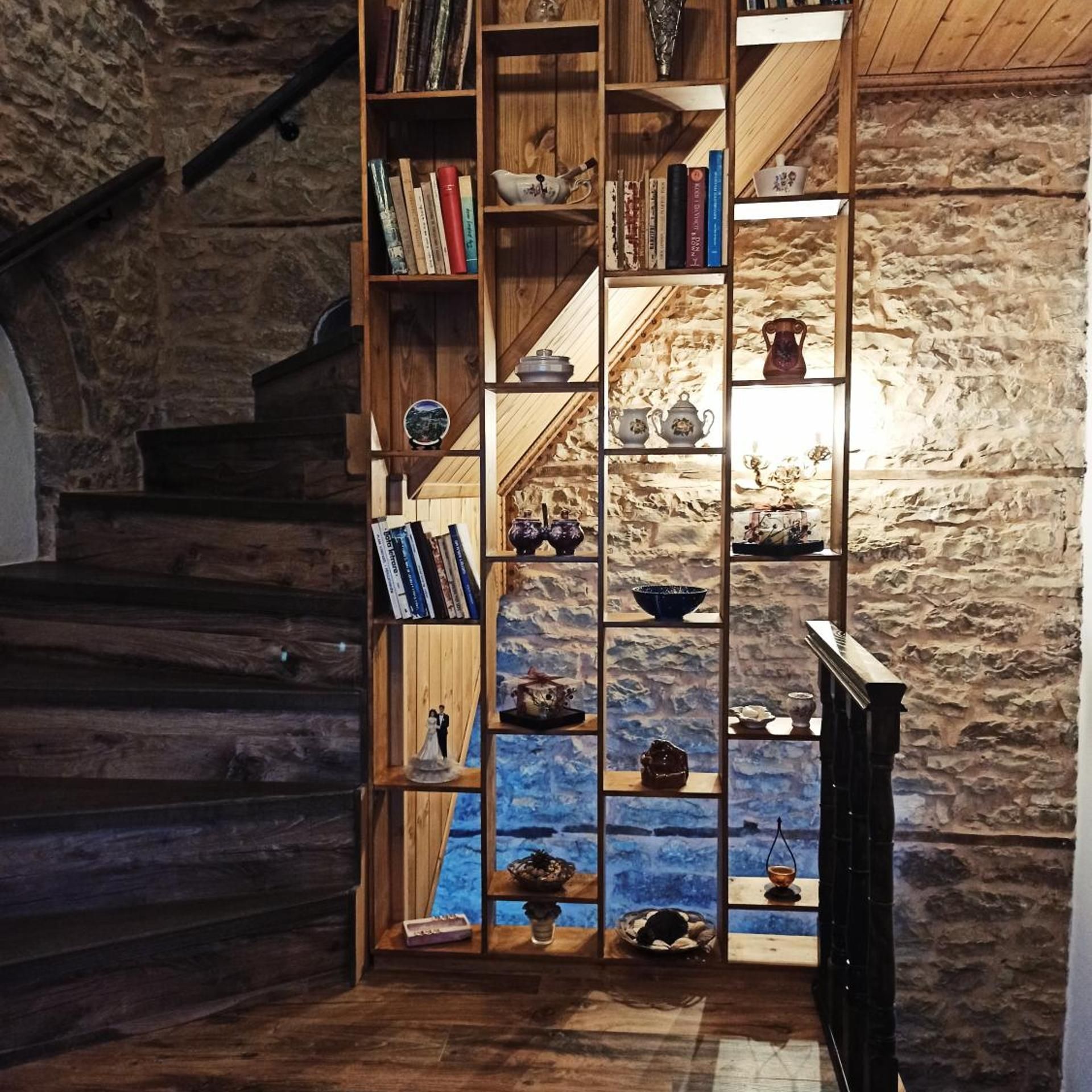 Eine Treppe mit Holzbalkon, die zu einem Raum mit Steinwand und einer Bücherwand voll mit Büchern und Dekorationsobjekten führt.
