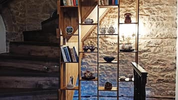 Eine Treppe mit Holzbalkon, die zu einem Raum mit Steinwand und einer Bücherwand voll mit Büchern und Dekorationsobjekten führt.