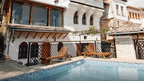 Ein Poolbereich mit Holzliegen, einem gefliesten Pool und einem weißen Gebäude mit mehreren Fenstern und Balkonen.