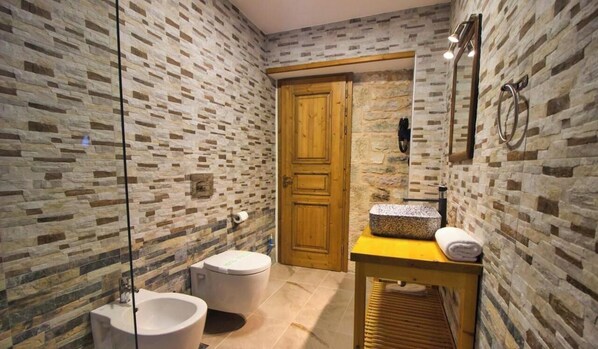 A bathroom with a stone wall, a wooden door, a sink with a granite countertop, and a mirror. - Hotel Praga (Gjirokastër)