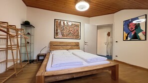 A bedroom with a wooden bed, a wooden headboard, a wooden floor, a ceiling light, a door, and a wall with a framed picture.