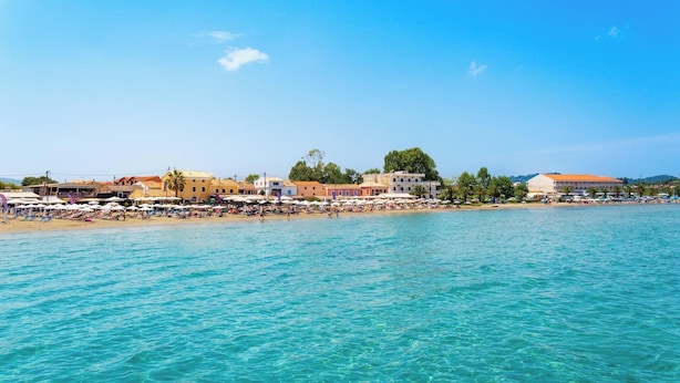 Un poble costaner amb una platja, edificis i aigua cristal·lina blava.
