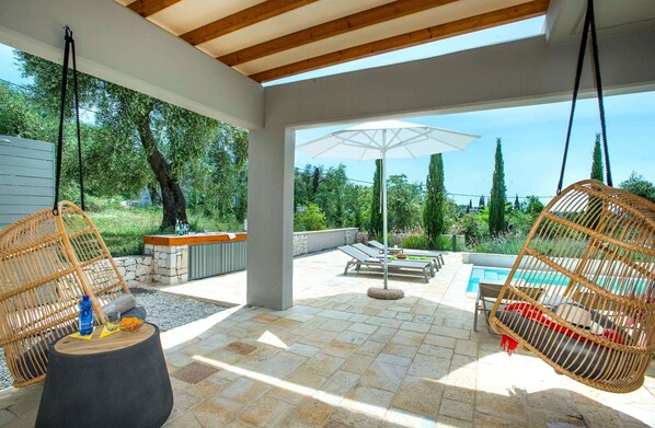 An outdoor patio with a pool, wicker chairs, a table, and a hanging swing.