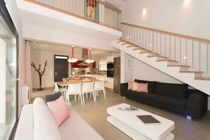 A modern living room with a sofa, a coffee table, a dining area with a table and chairs, and a staircase leading to an upper floor.