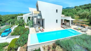 Una vila moderna amb piscina, envoltada de vegetació exuberant i una vista despejada de les muntanyes.