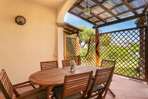 A round wooden table with six chairs, a decorative vase, and a lattice door leading to a garden.