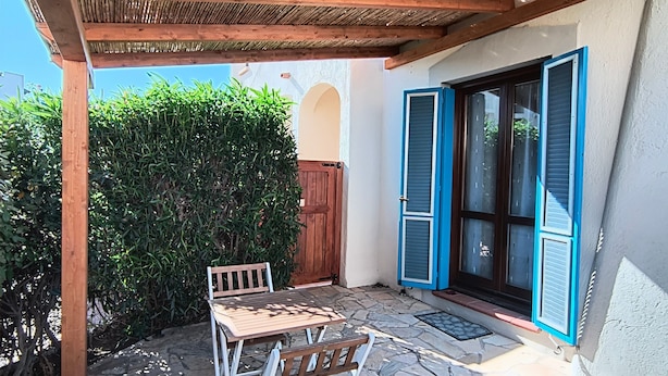 Une terrasse dotée d’une pergola en bois, d’une table en pierre et de chaises.