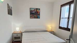 Une chambre à coucher avec un lit, deux tables de chevet avec des lampes, un tableau accroché au mur et une fenêtre avec des rideaux.