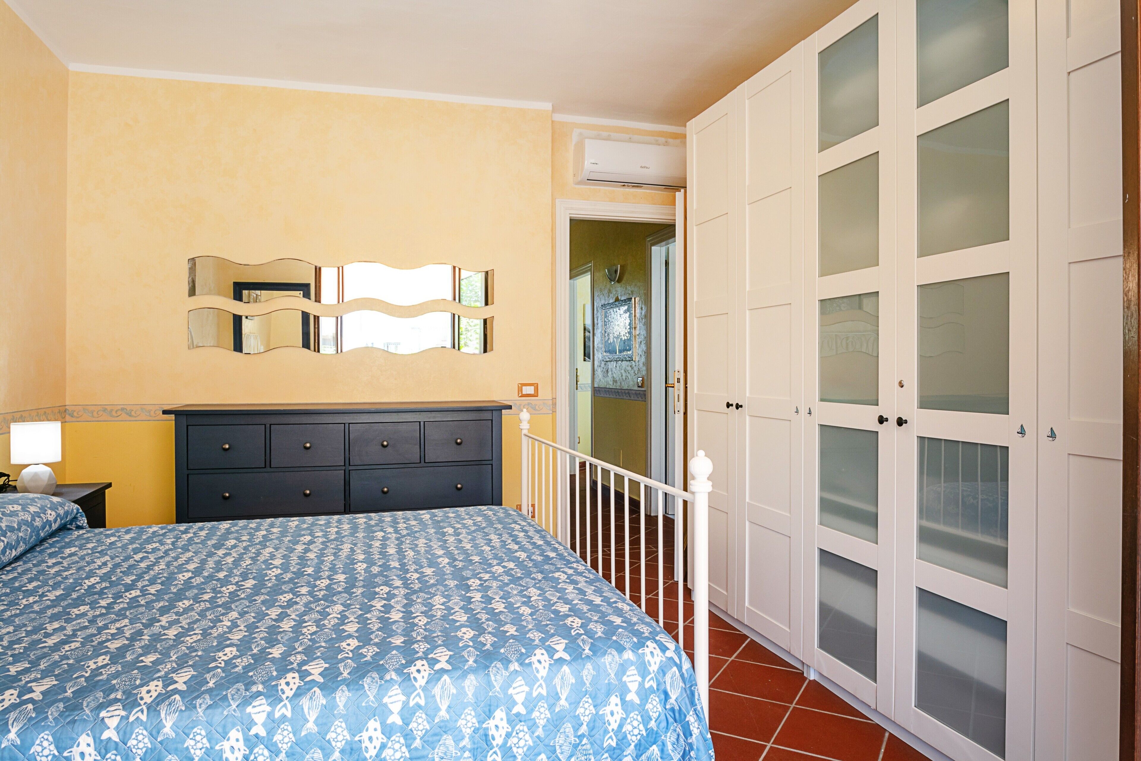 Ein Schlafzimmer mit einem Bett, einer Kommode, einem Spiegel und einem Kleiderschrank mit Milchglasschränken.