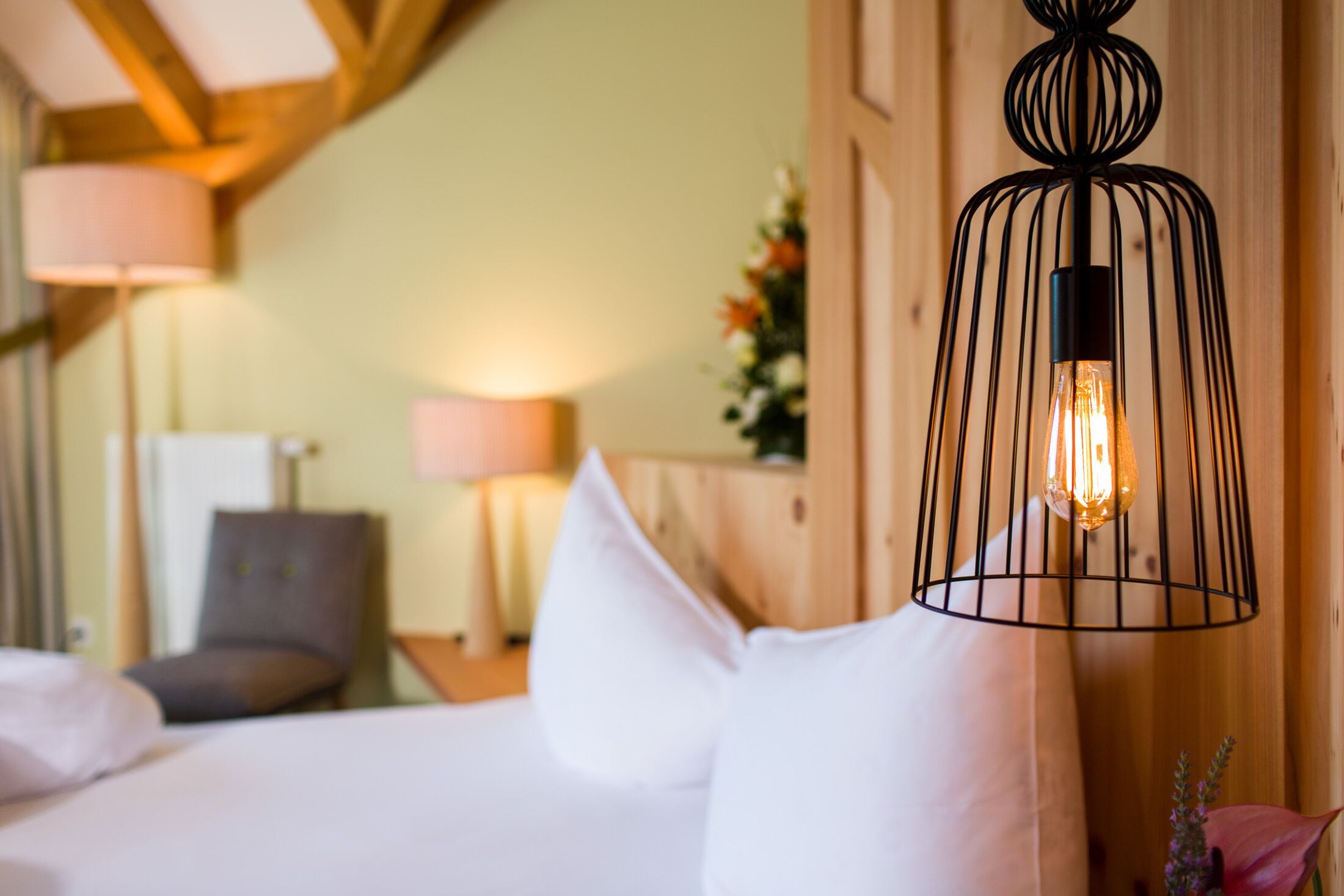 A hotel room with a bed, a chair, a lamp, and a decorative plant.