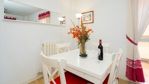 A dining area with a white table, four chairs, a vase with flowers, a wine bottle, and a framed picture on the wall. - Apartment 'Alborada Golf  1A' with Terrace, Shared Pool & Wi-Fi (Alfaz del Pi)