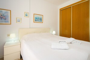 Une chambre d’hôtel avec un lit, une table de chevet avec une lampe, une armoire en bois et trois tableaux encadrés accrochés au mur.