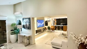 A modern living room with a sofa, a dining area with chairs, a TV, and a kitchen area with a TV and cabinets. - Villa Vega with Pool, Garden & Wi-Fi (Alfaz del Pi)