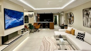 A modern living room with a large flat-screen TV, a sofa, a coffee table, and a dining area with chairs. - Villa Vega with Pool, Garden & Wi-Fi (Alfaz del Pi)