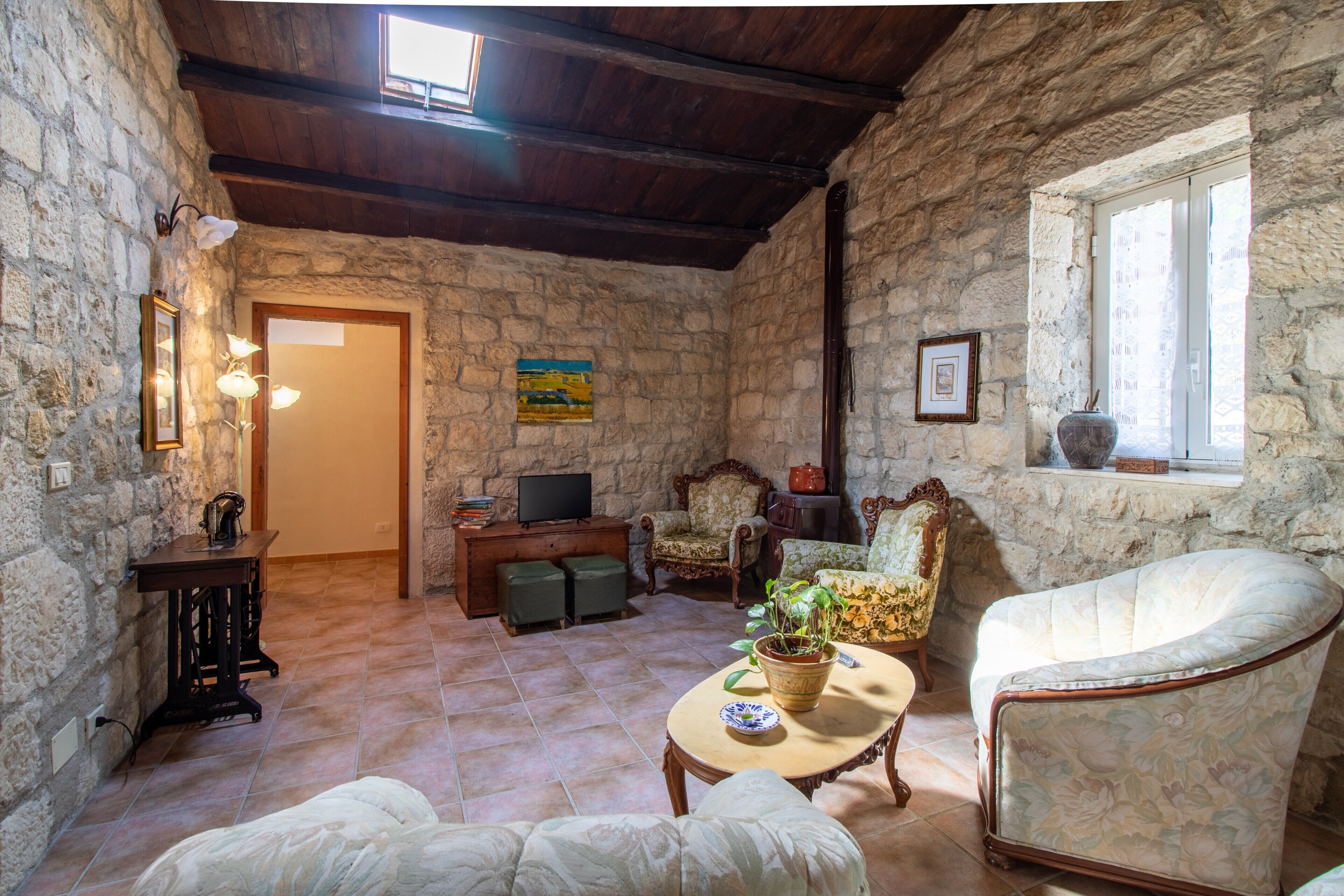 Una habitación con paredes de piedra y techo de madera, un televisor, un sofá, una silla y una mesa con una planta.