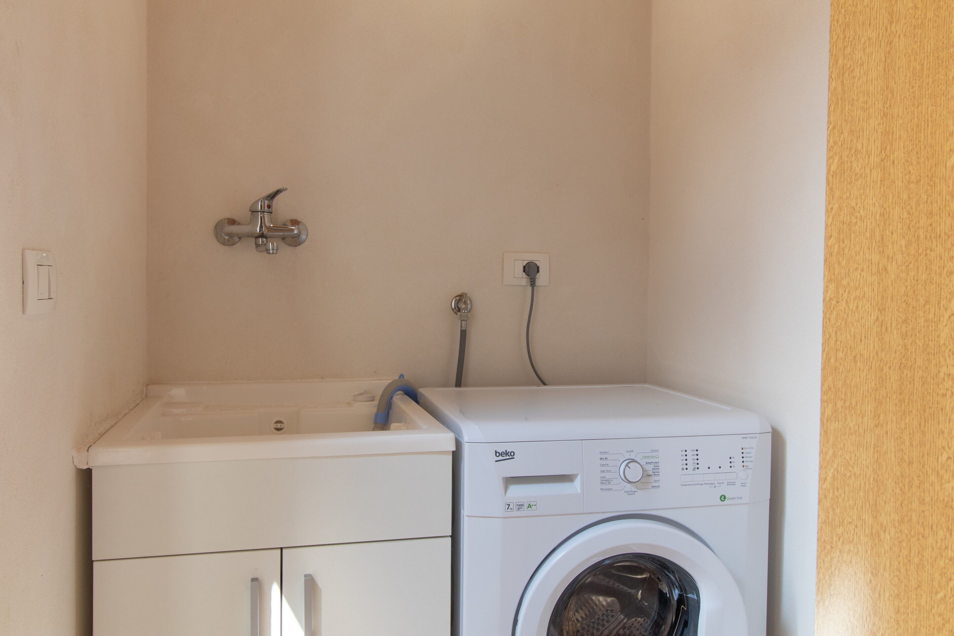 Un espace buanderie compact comprenant un lave-linge, un évier et un robinet.