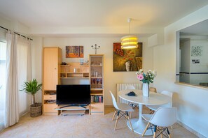Una sala de estar moderna con un televisor de pantalla plana, una mesa de comedor con sillas, una estantería y una planta en maceta.