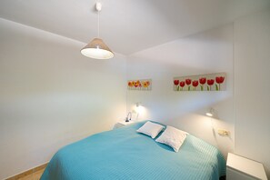 Un dormitorio con una cama, una mesita de noche, una lámpara de pared y dos cuadros con flores.