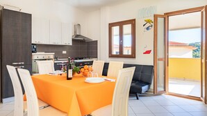Un coin repas avec une table dressée pour quatre personnes, une cuisine équipée d’appareils modernes et un balcon avec vue.