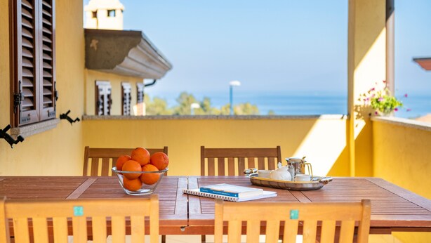 Une table en bois sur laquelle se trouvent un saladier rempli d’oranges, un carnet et un plateau avec du pain et une carafe.
