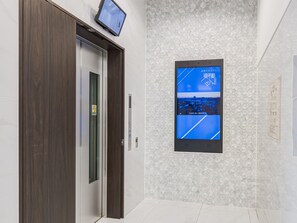 An elevator with a digital display and a wall-mounted screen showing a cityscape. - Toyoko Inn Oyama Eki Higashi-guchi 2 (Oyama)