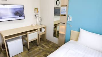 A hotel room with a bed, a desk with a chair, a small refrigerator, a clock, and a television displaying a news channel.