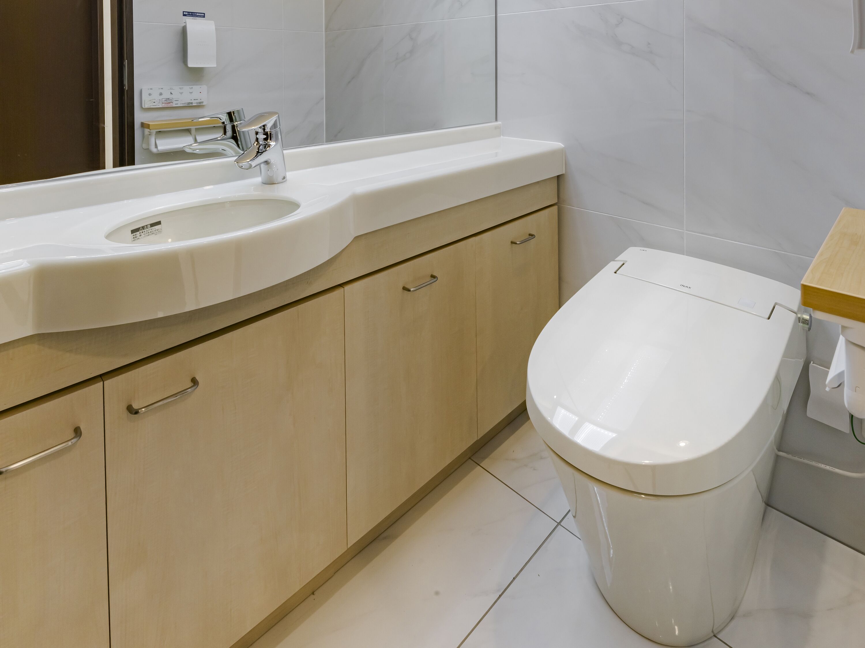 A modern bathroom with a white sink, a chrome faucet, wooden cabinets, and a white toilet.