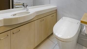 A modern bathroom with a white sink, a chrome faucet, wooden cabinets, and a white toilet.
