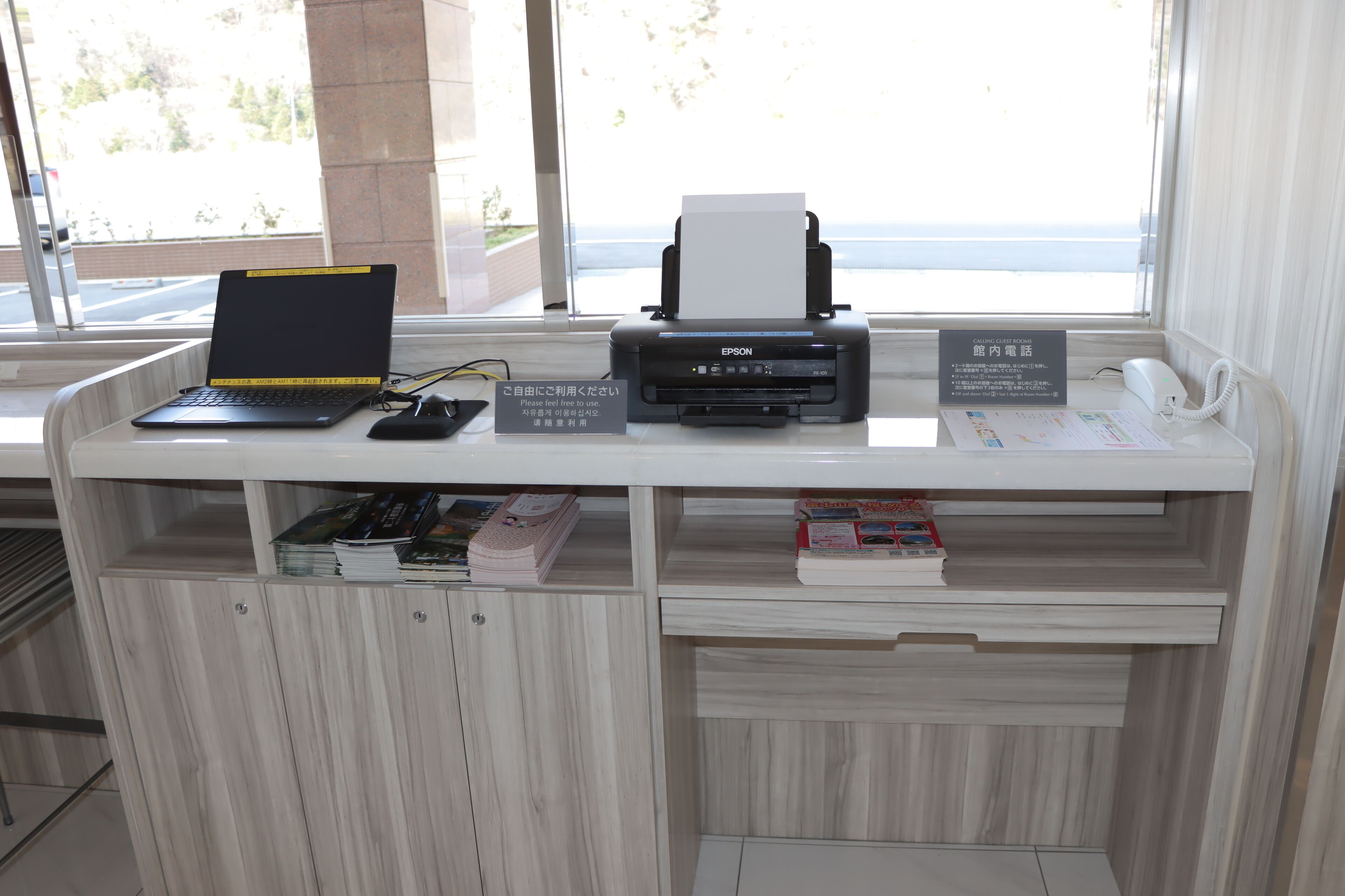 A reception desk with a laptop, a printer, a phone, and a sign in a foreign language.