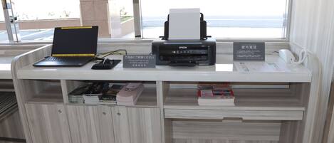A reception desk with a laptop, a printer, a phone, and a sign in a foreign language.