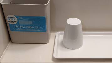 A trash bin with a recycling label and a white cup on a tray.