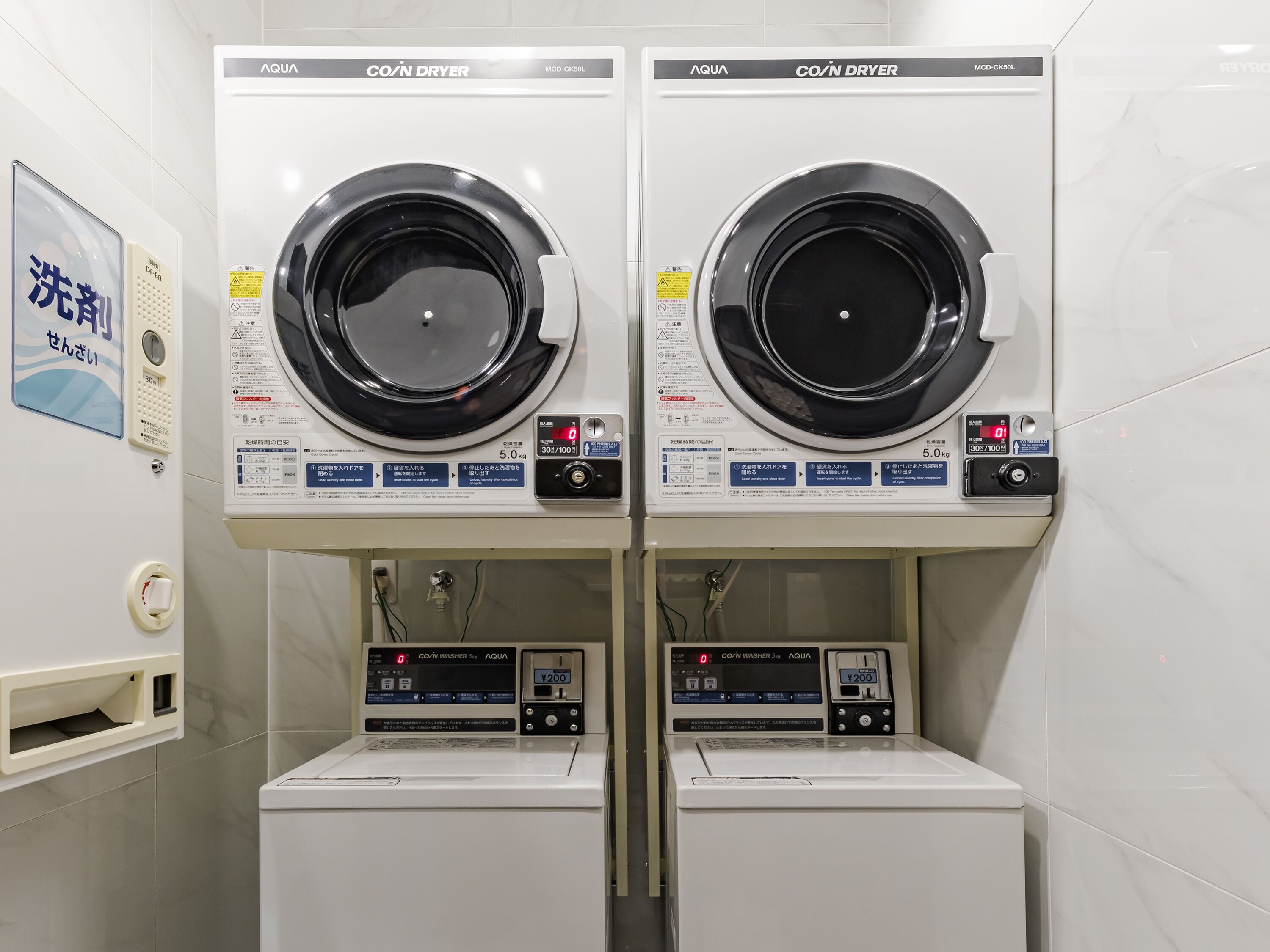 Deux machines à laver à chargement frontal identiques, dotées d’écrans numériques, sont placées côte à côte dans une pièce propre, dont le sol est carrelé.