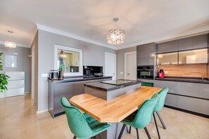 Une cuisine moderne dotée d’un îlot central, d’un coin repas avec des chaises vertes et d’un luminaire suspendu.
