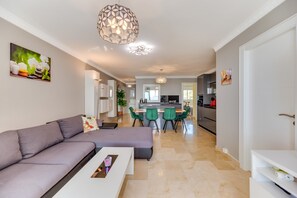 Un salon moderne avec un canapé, une table à manger et des chaises, une cuisine en arrière-plan et un luminaire suspendu.