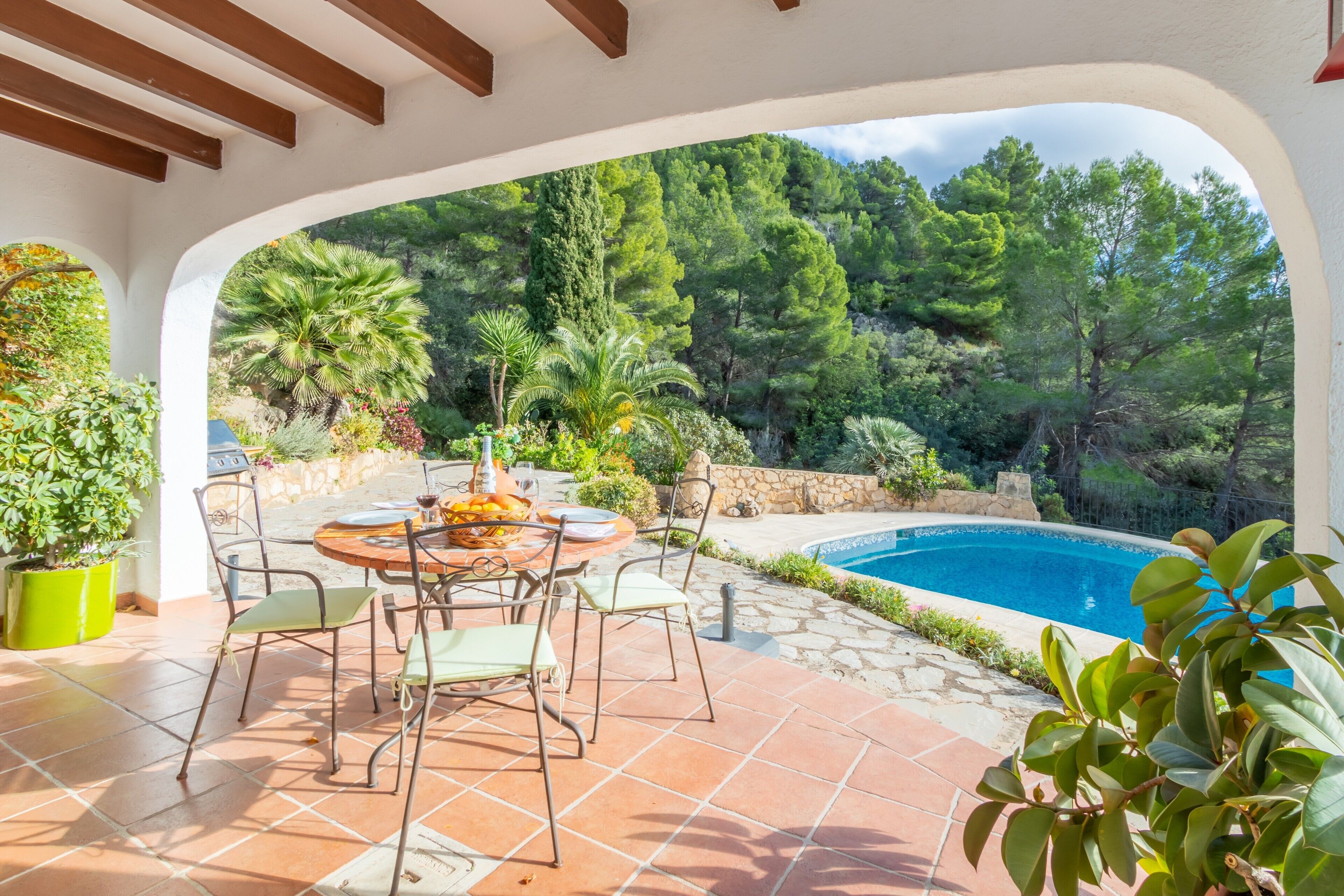 Un patio exterior con piscina, rodeado de exuberante vegetación y un muro de piedra.