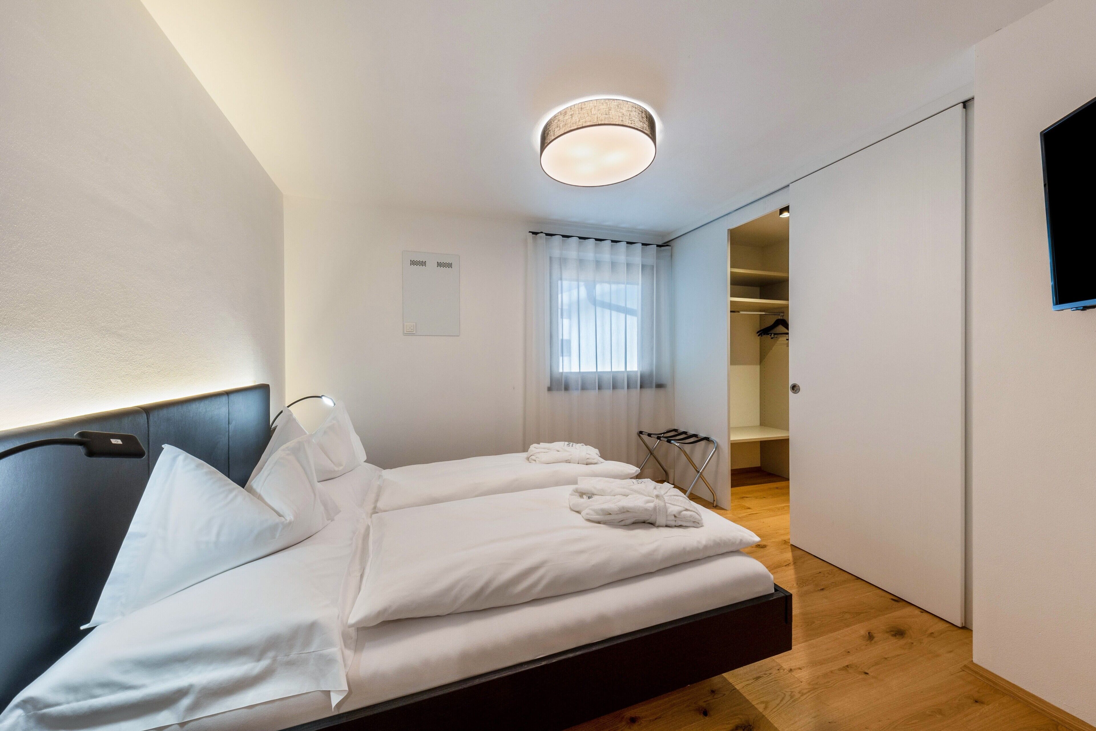 Een moderne hotelkamer met een bed, nachtkastje, een aan de muur bevestigde televisie en een raam met gordijnen.
