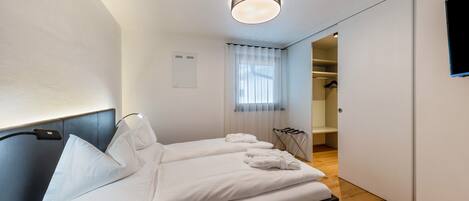 Een moderne hotelkamer met een bed, nachtkastje, een aan de muur bevestigde televisie en een raam met gordijnen.