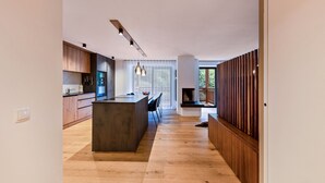 A modern kitchen with wooden cabinets, a central island, pendant lighting, and a view of the outdoors through large windows. - UB31 Holiday Apartment – Exclusive Apartment with Private Wellness Oasis (Deutschnofen)