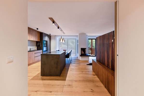 A modern kitchen with wooden cabinets, a central island, pendant lighting, and a view of the outdoors through large windows.