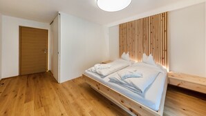 A modern bedroom with a wooden bed, a built-in headboard, and a ceiling light fixture. - UB31 Holiday Apartment – Exclusive Apartment with Private Wellness Oasis (Deutschnofen)