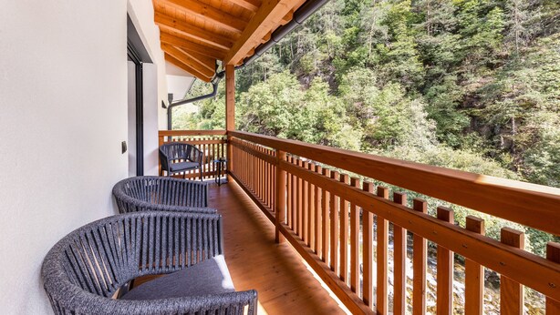 A wooden balcony with two wicker chairs, overlooking a forested hillside. - UB31 Holiday Apartment – Exclusive Apartment with Private Wellness Oasis (Deutschnofen)